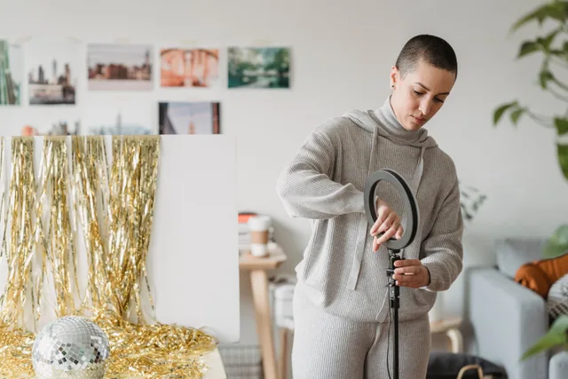 Young focused female in hoodie installing professional lamp against frippery and decorative ball in house room. Launching a photo booth rental business into a real market