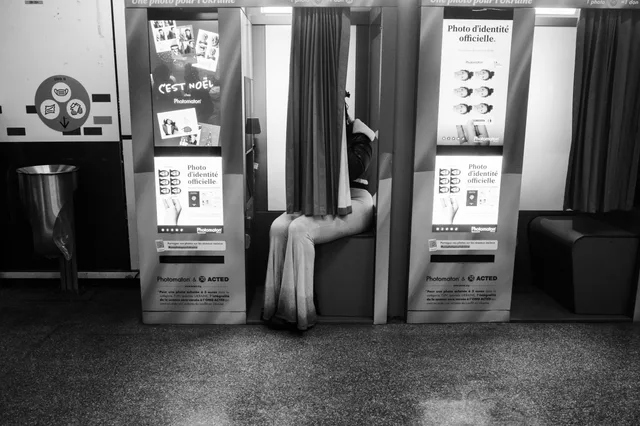 A person sitting inside a photo booth enclosed by curtains in a public space. What it costs to start a photo booth rental business, and where the money comes from