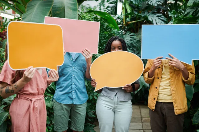 A group of adults holding colorful speech bubble signs in a lush greenhouse setting. Bilingual photo booth prop kits and templates for Quebec and Ottawa events